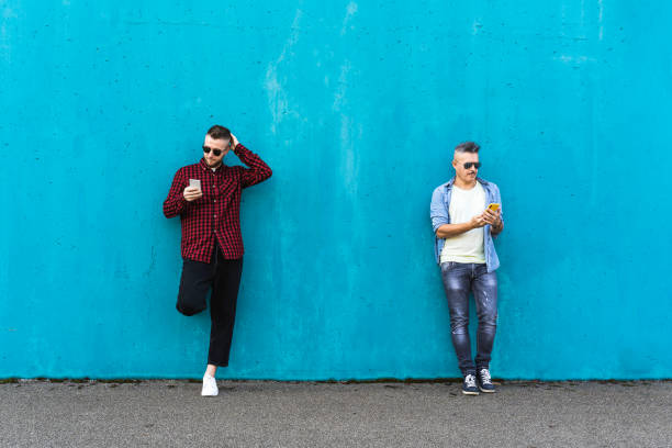 Cool men looking at mobile phone lean against blue wall outdoors - Couple of friends addicted to technology and social networks - Concept of tech, social network and social relationships Cool men looking at mobile phone lean against blue wall outdoors - Couple of friends addicted to technology and social networks - Concept of tech, social network and social relationships italian music stock pictures, royalty-free photos & images