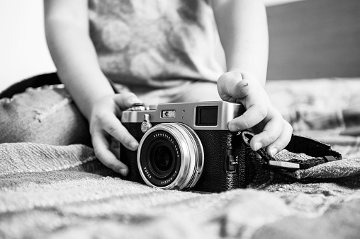 Close up of a mirrorless retro camera on the blanket - Little girl playing with camera - Talented little girl has fun with vintage camera at home - Leisure activity at home - Black and White