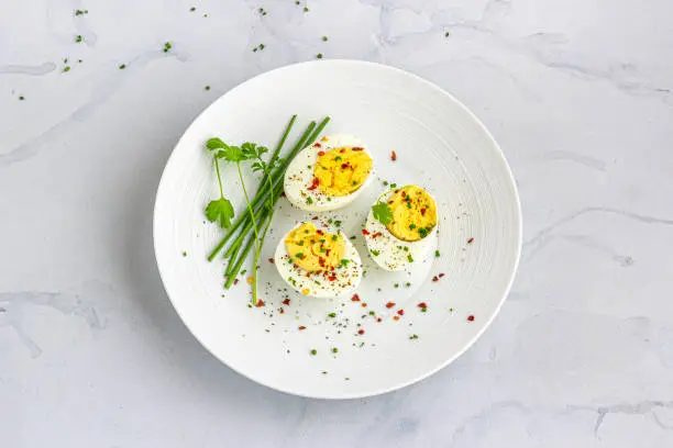 Sliced Boiled Eggs on a White Dish with Sprinkled Black Pepper, Chili Flakes and Chives Top Down Flat Lay Photo