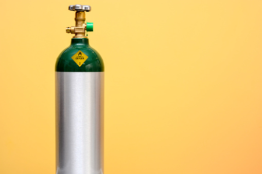 Green and silver medical oxygen tank isolated on yellow background