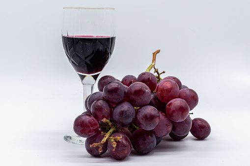Wine glass with bunch of red grapes on white background.  Fresh fruit.  Red wine