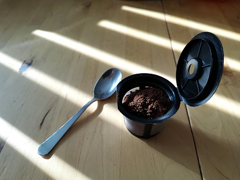 Close-up of a reusable coffee pod, freshly filled with ground coffee, on a kitchen table.