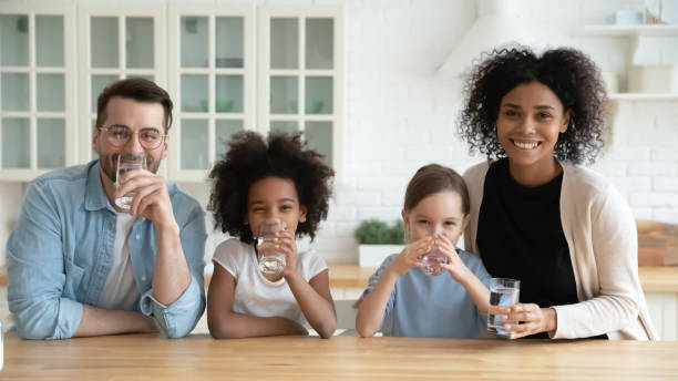 Happy multiracial family drinking pure mineral water in kitchen Portrait happy multiracial family drinking pure mineral water in kitchen, smiling African American mother and Caucasian father with two little daughters enjoying fresh aqua, healthy lifestyle concept pure race stock pictures, royalty-free photos & images