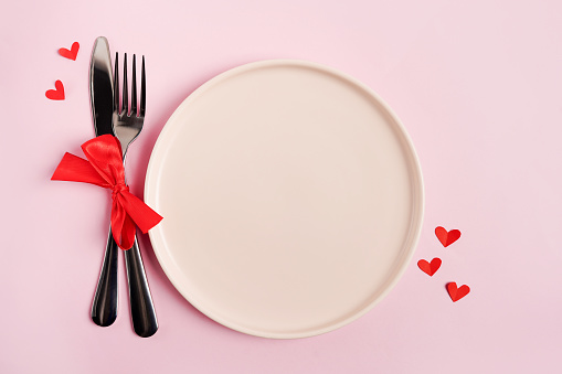 Festive table setting for Valentines Day with empty plate on pink table with red hearts