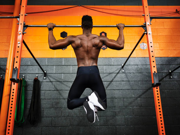 Man Working Out in a Gym Doing Pull-ups Man working out in a gym doing pull-ups on a bar. chin ups photos stock pictures, royalty-free photos & images