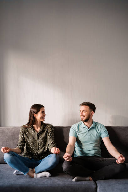 istock Man and woman sitting on sofa in lotus pose 1294924489