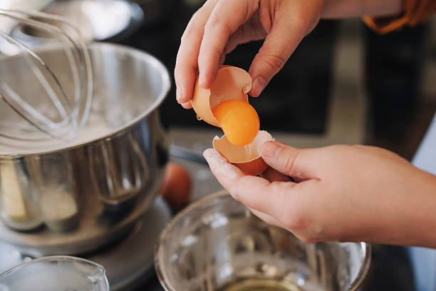 케이크를 만드는 동안 금속 그릇 위에 달걀 흰자에서 달걀 노른자를 분리하는 익명의 젊은 여성 - groceries food cake domestic kitchen 뉴스 사진 이미지