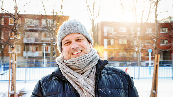 Mature man dressed for deep Winter urban portrait back lit by sunset. he is wearing a tuque and a heavy scarf.