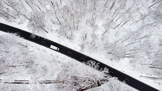 Road through snow-covered forest - aerial view. Unrecognisable truck