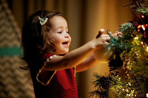 Happiness decorating the Christmas tree, baby girl holding Christmas decorations and ornamanets