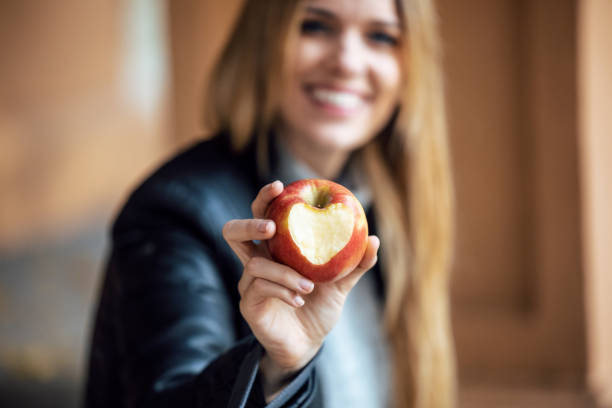 Beautiful smiling woman having fun while showing an apple with a heart looking at camera in the park. Shot of beautiful smiling woman having fun while showing an apple with a heart looking at camera in the park. apple bite stock pictures, royalty-free photos & images