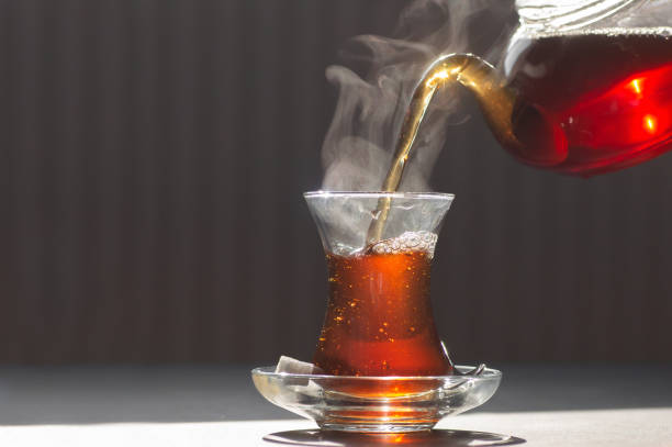 Glass cup of brewed black turkish tea, traditional hot drink concept Glass cup of brewed black turkish tea pouring from teapot, traditional hot drink concept black tea stock pictures, royalty-free photos & images