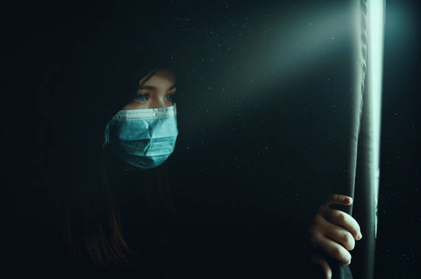 Girl with protective mask looking on the window in darkness