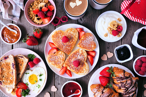 Escena de la mesa de desayuno del Día de San Valentín o madres sobre un fondo de madera oscura con tortitas en forma de corazón, huevos y comida temática del amor photo