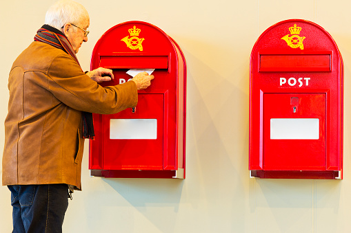 Senior man in brown leather jacket posting a letter in a Danish mailbox
