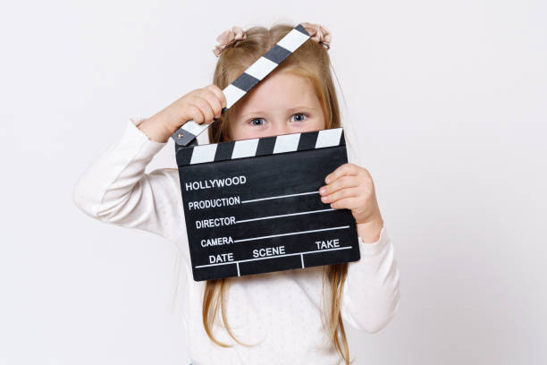istock A girl looks through a clapperboard into the camera. Isolated over white background. 1294944511