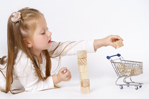Children concept. The girl lies on the floor and plays with a mini cart and cubes. Isolated over white background.