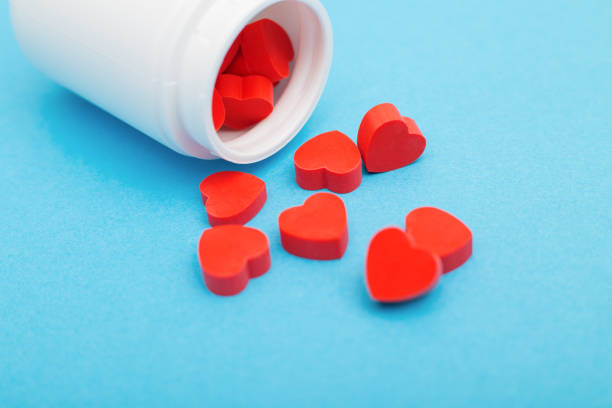 czerwone tabletki w kształcie serca z plastikową butelką na niebieskim tle. pojęcie uzależnienia od miłości, narkotyków miłości, walentynki i depresja - red wine zdjęcia i obrazy z banku zdjęć