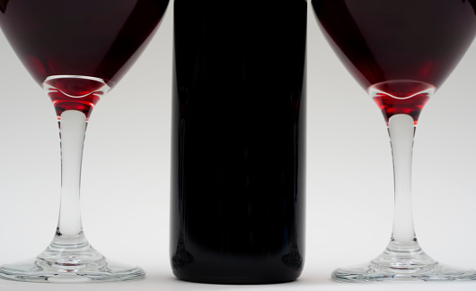 close shot, red wine, 3/4 view of bottle and 7/8 view of glasses, glasses full of red wine, white background, glasses even with bottle, no people