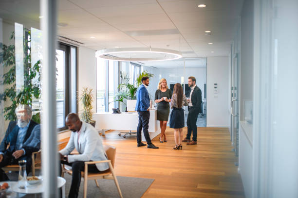 Business Associates Relaxing on Break from Corporate Seminar Personal perspective of relaxed business executives enjoying conversation and a break from seminar in office lobby. personal perspective standing stock pictures, royalty-free photos & images