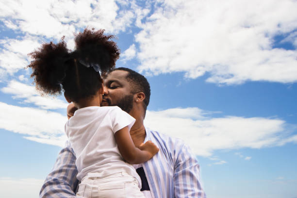 African American father hugging his daughter with blue sky clound background African American father hugging his daughter with blue sky clound background african father stock pictures, royalty-free photos & images