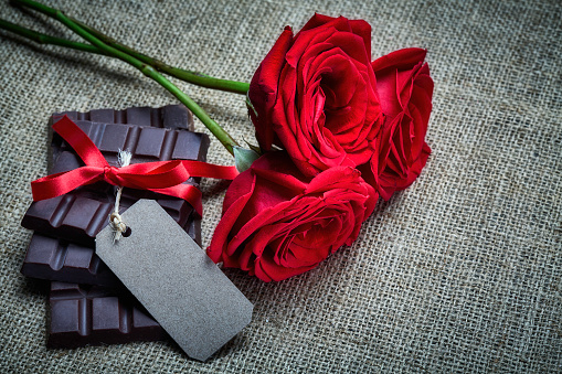 Valentine's Day theme: Red roses with chocolate bars and a blank cardboard on a rustic table