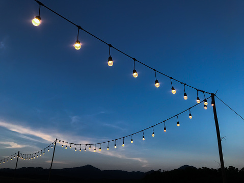 Light bulbs hang overhead on a dark blue sky in the evening.
