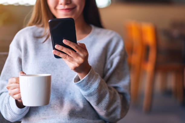 istock a beautiful young asian woman holding and using mobile phone while drinking coffee 1294974316