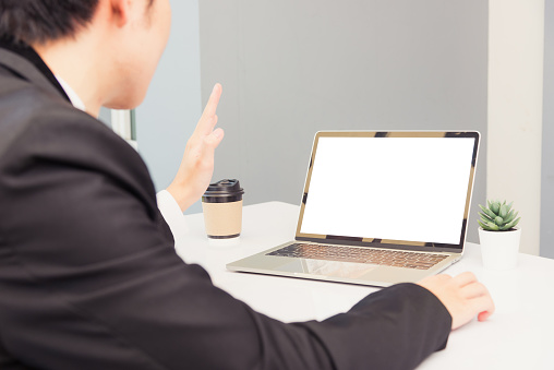 Work from home, Asian young businessman smile wearing suit video conference call or facetime by laptop computer raise your hand to say hello on desk at home office