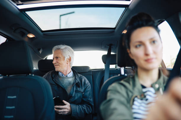 uomo anziano in sella con un autista di carshare femminile - driving senior adult car women foto e immagini stock