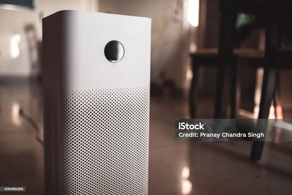 Close up of an air purifier placed indoors in a living room of the house. White air purifier placed in the living room inside a house with copy space. Home pollution control and air purification system to remove air borne pollutants. HEPA Filter Stock Photo