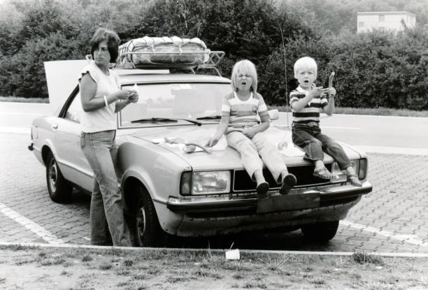 Young mother with daugter and son on a roadtrip in Germany. Vintage monochrome 1978 image; young mother with daugter and son sitting on hood of car eathing lunch sausages on a roadtrip holiday in Germany. 1970s woman stock pictures, royalty-free photos & images