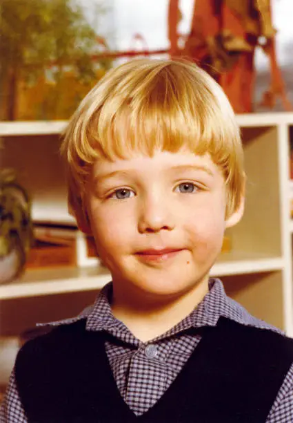 Vintage 1977 yearbook school image of a smiling young boyl with blond hair and blue eyes with blue spencer and blouse.