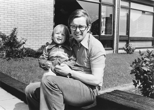 1975 vintage, seventies, retro monochrome portrait of father and daughter sitting in front of a house in the summer sun.