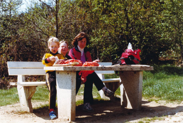 Vintage retro young mother with son and daughter eating lunch Vintage colorful 1979 roadtrip image of a young mother with son and daughter sitting at picnic table and eating a sandwich on a parking on the German highway. picnic photos stock pictures, royalty-free photos & images