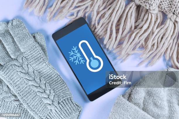 Concept For Cold Temperatures With Snow And Minus Degrees With Mobile Phone Showing Weather Forecast Surrounded By Warm Clothes Stock Photo - Download Image Now
