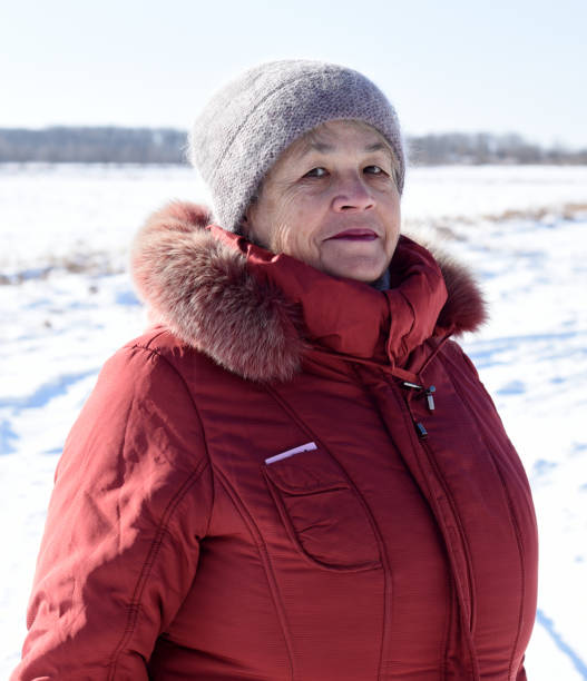 ritratto di donna anziana russa in berretto che guarda la telecamera contro il campo innevato. inverno - russian ethnicity cold relaxation nature foto e immagini stock