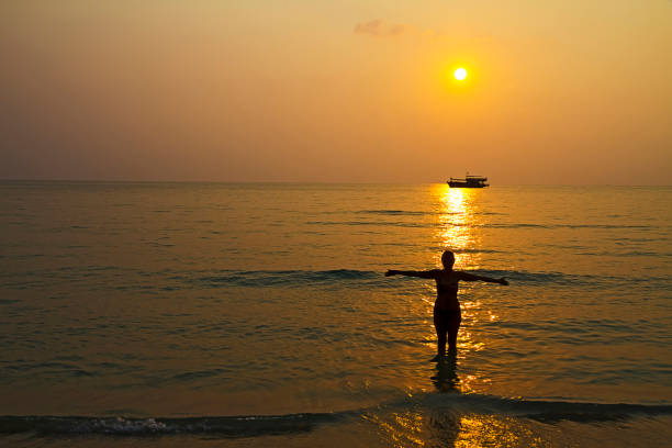 istock Sunset and silhouette woman in wave on beach 1294990864