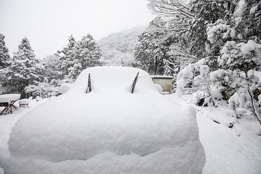 A front on view of a car totally covered in a thick layer of snow with only the windshield wipers poking out.