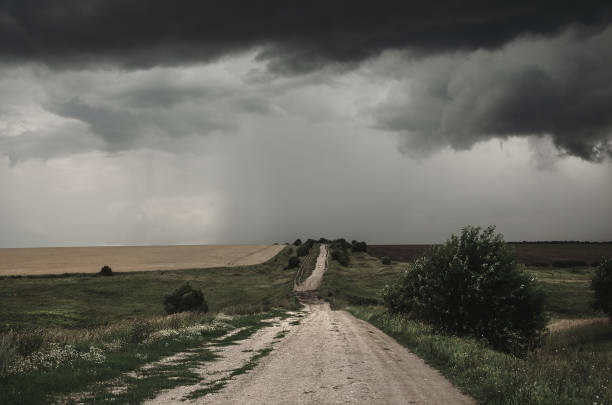 istock Cloudy summer landscape with ground country road passing through the fields on a background of dark overcast sky. 1294991919