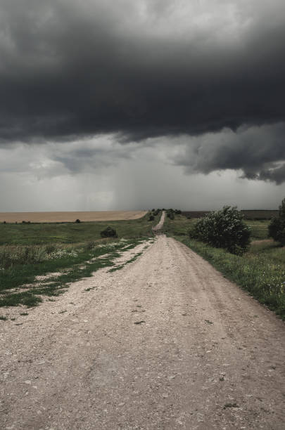 istock Cloudy summer landscape with ground country road passing through the fields on a background of dark overcast sky. 1294991926