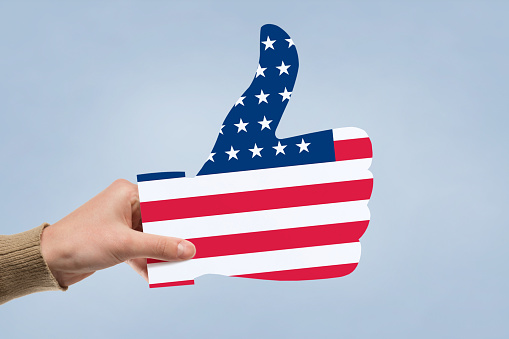 Hand holding American flag in shape of thumb. US elections concept.