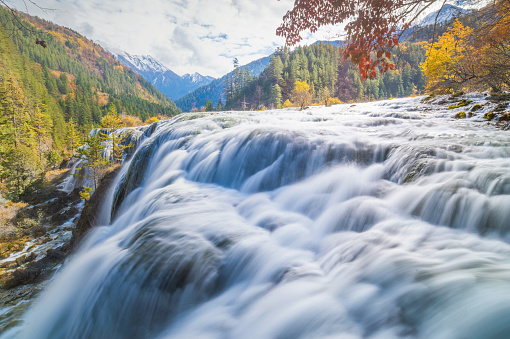 Pearl Shoals Waterfall among scenic wooded mountains and evergreen forest in Jiuzhaigou nature reserve