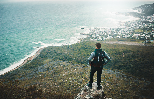 Shot of a young man looking at the view from a cliff while out on a hike