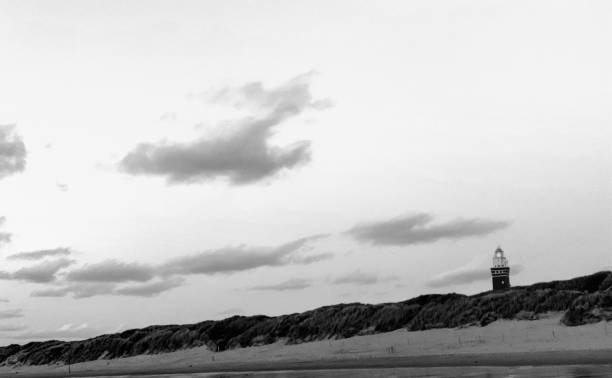 istock Lighthouse standing on the Dutch coast with a dramatic sunset or sunrise sky behind it in Monochrome 1295002560