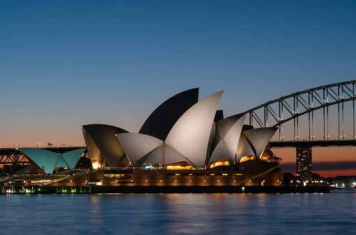 Sydney, Australia - August 3, 2019: Evening descends upon Sydney, and the twin icons of Sydney Harbour, the Opera House and the Harbour Bridge, stand out against a dramatic sky.