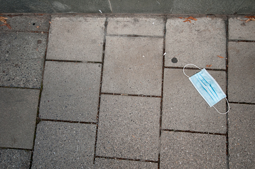 A light blue mouth and nose mask lying on the pavement.