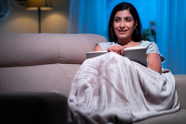 istock young women reading book at home sitting on sofa 1295005354