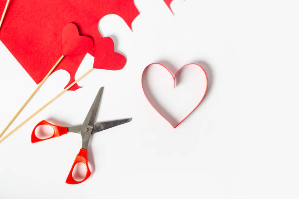 istock Red heart cut from paper, scissors and colored cardboard on a light white background. Composition Valentine's Day. Banner. Flat lay, top view 1295005365