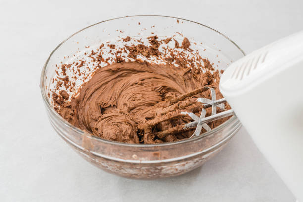 istock Chocolate buttercream icing preparation process. Mixing ingredients in a glass bowl 1295006141